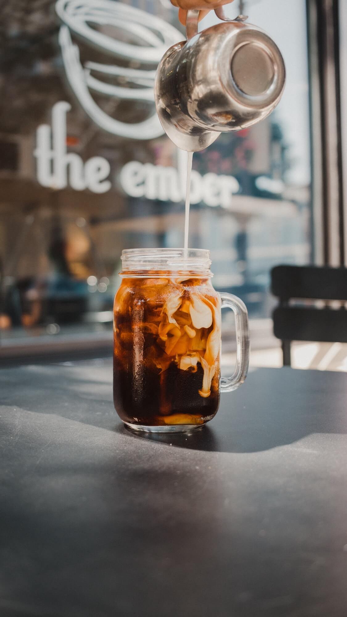 Cream being poured into a mason jar of cold brew coffee