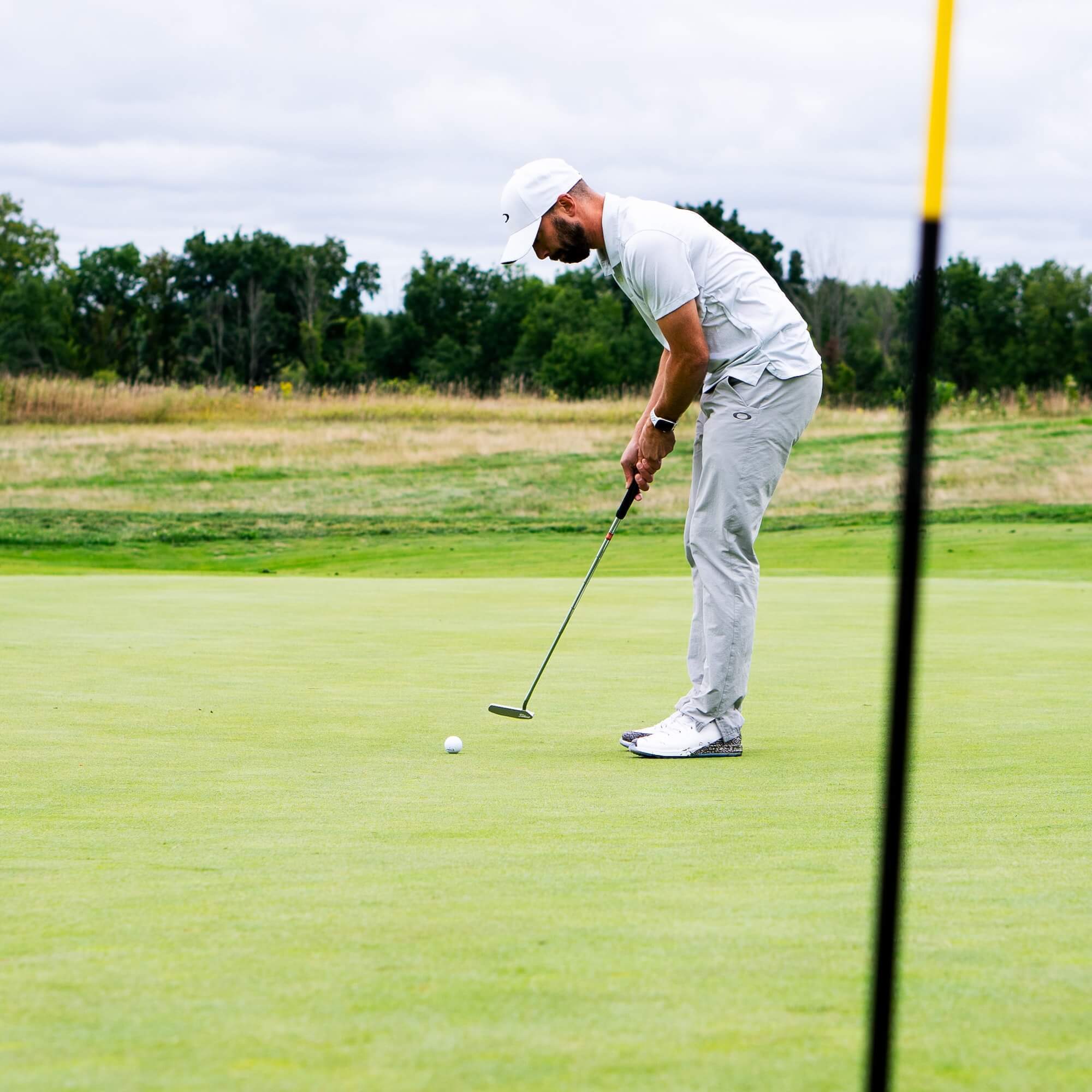 Man in white and grey golf clothing putts on the green