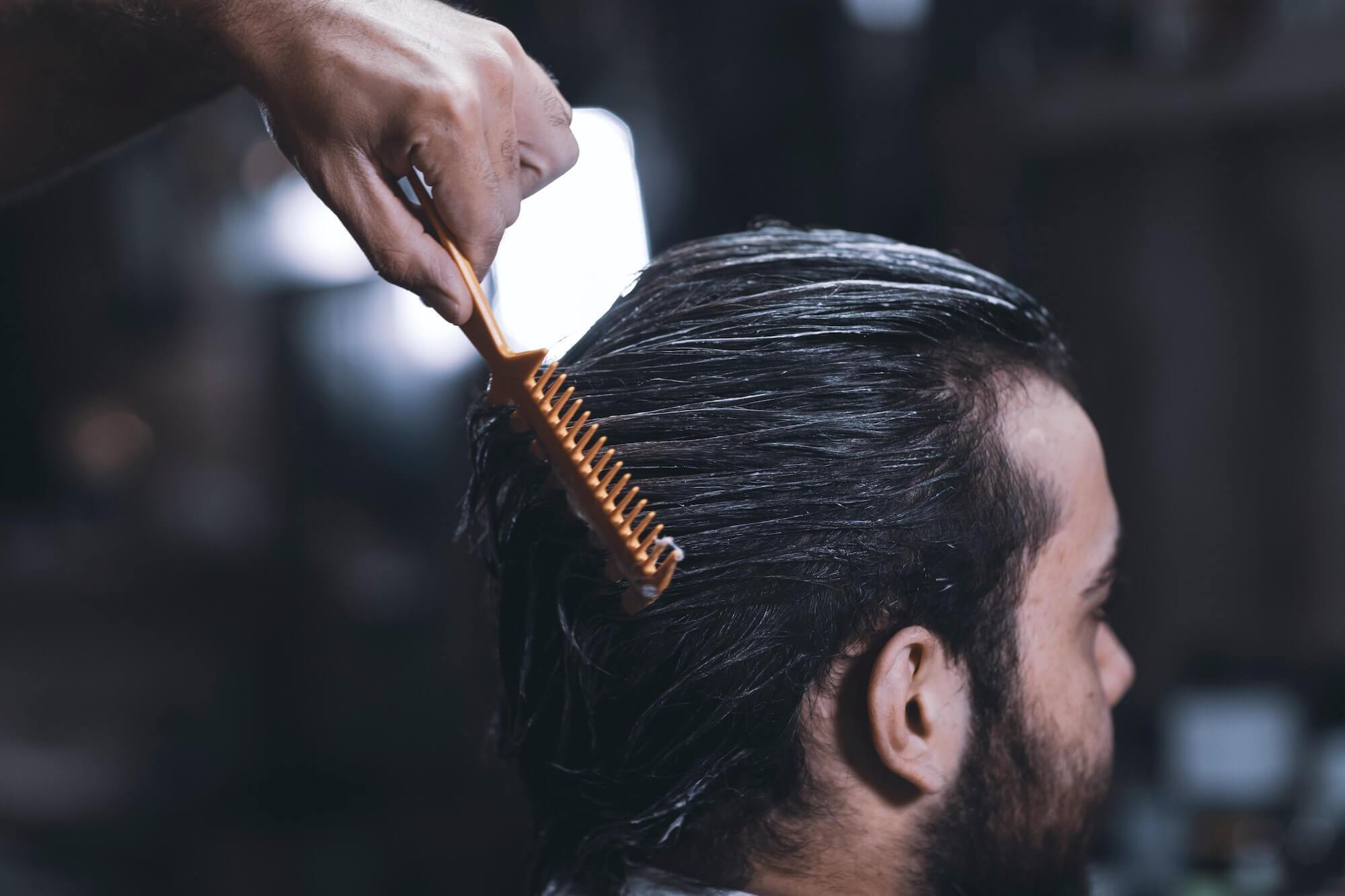 Barber combing hair product through man's brown hair