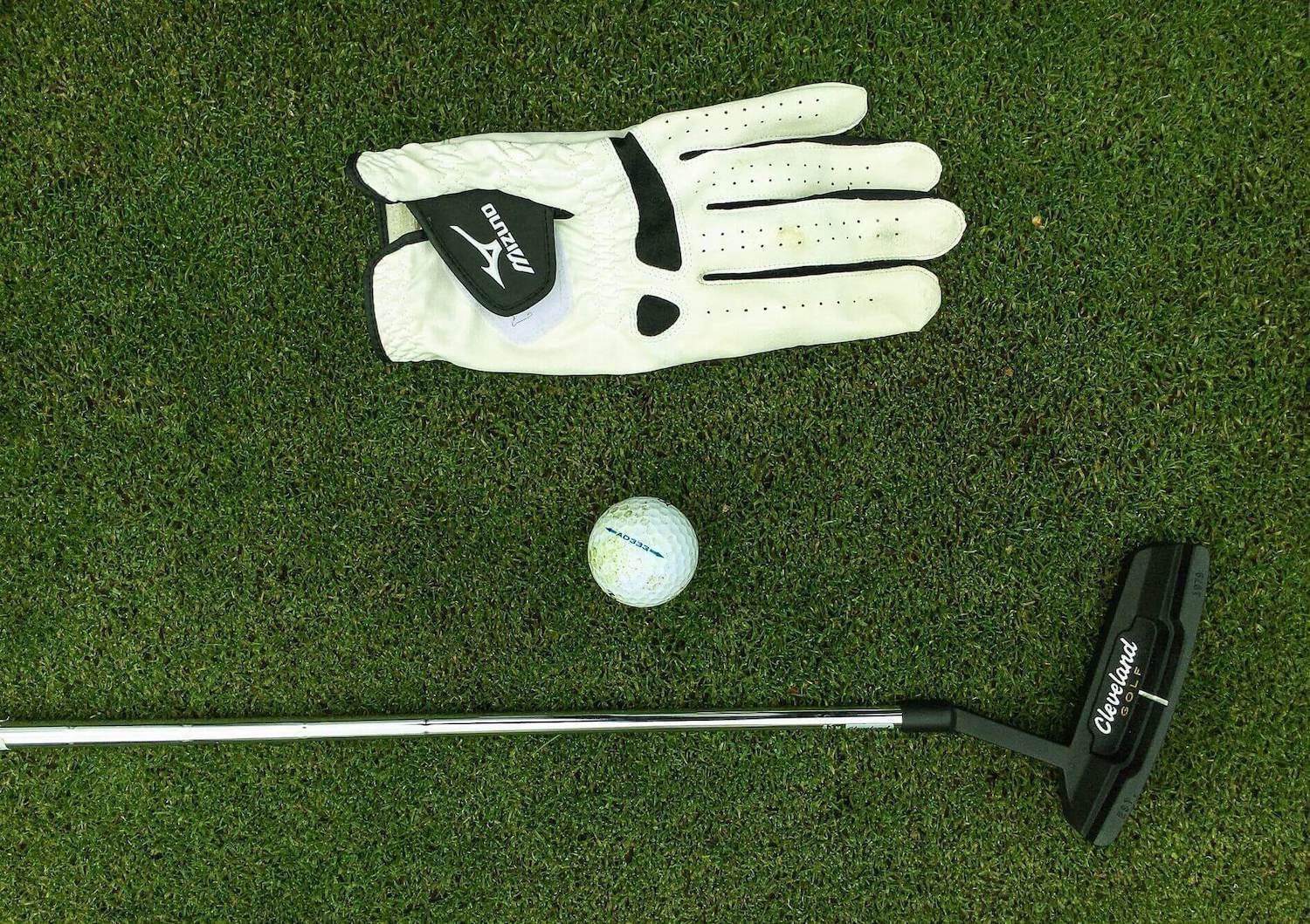 Mizuno golf glove, golf ball and Cleveland golf putter lying on golf course