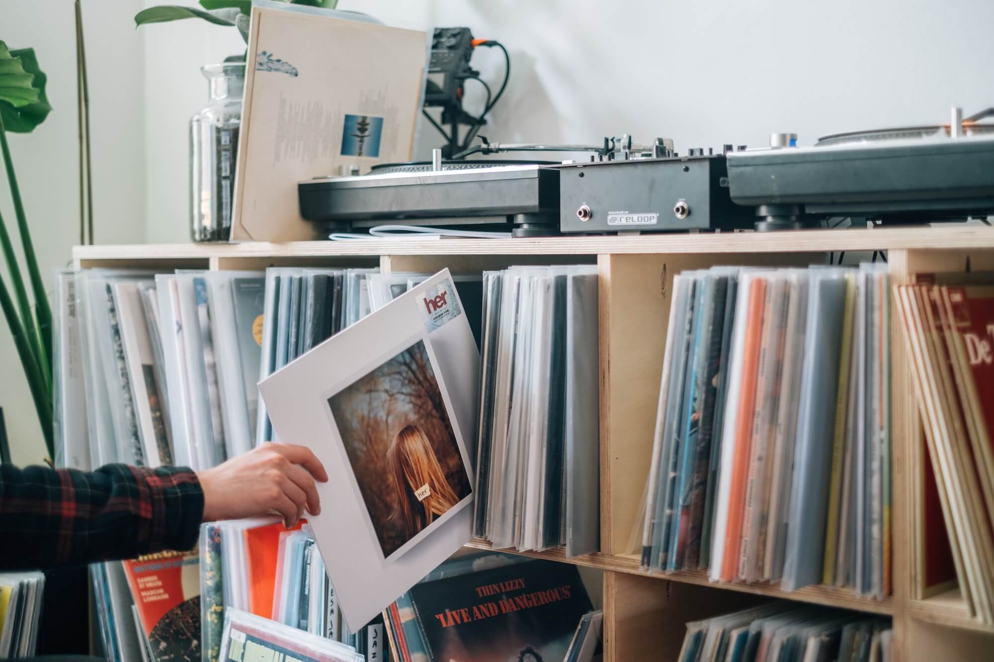 Person pulling record from vinyl collection held in shelving unit with turntable on top