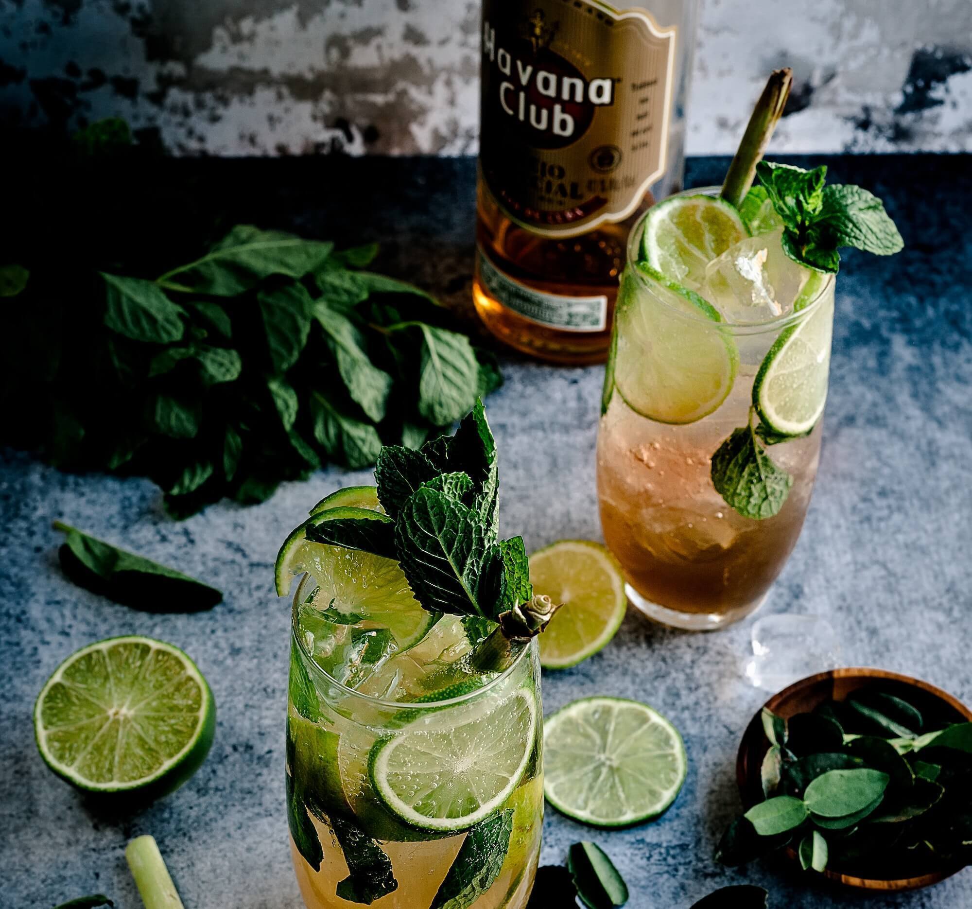 Bottle of Havana Club rum, mojito cocktails, mint and sliced lime on countertop