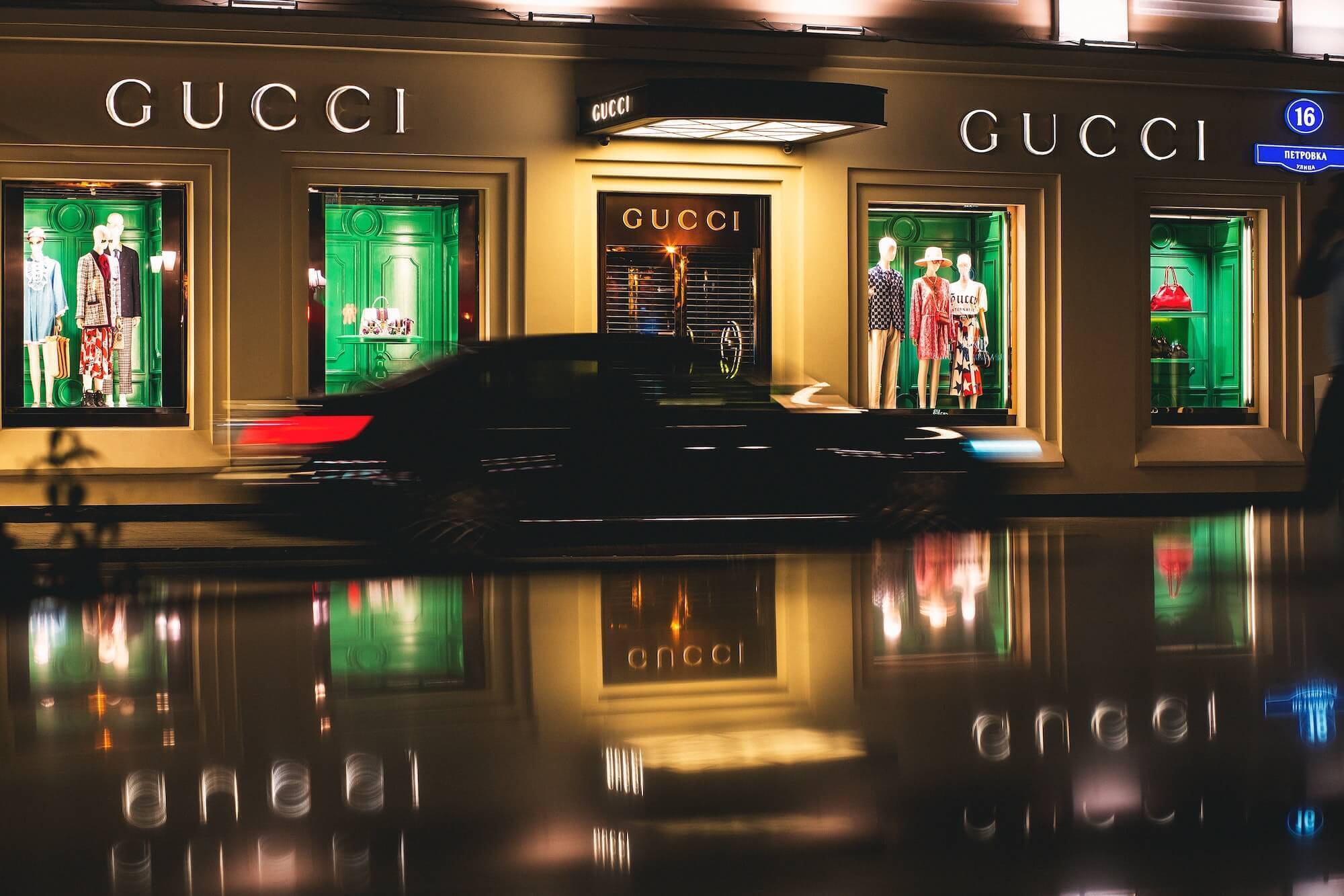 Nighttime shot of lit-up Gucci storefront with blurred moving car in front